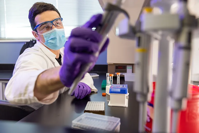 A scientist wearing personal protective equipment docks a tube into a testing machine.