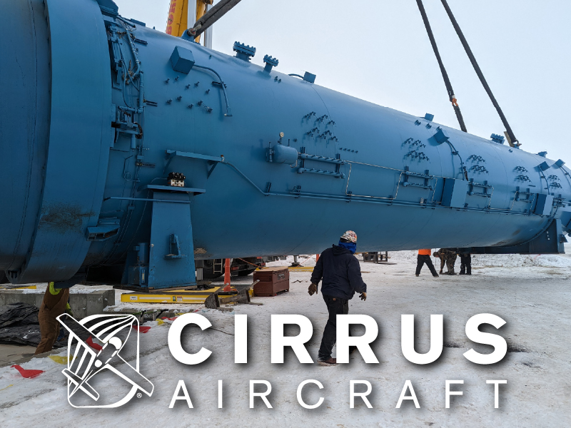 At Cirrus Aircraft manufacturing facility in Grand Forks, a large cylinder suspends from a crane at eye level as a person stands in front of it at 1/3 the size of the cylinder.