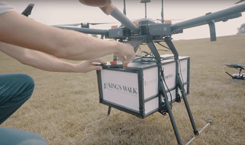 A person is loading up a drone compartment for a delivery on the Kings Walk Golf Course in Grand Forks North Dakota as part of a food delivery system. The drone is about 2.5 feet tall with a wing span of 5 feet.