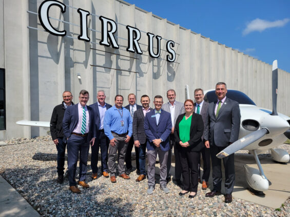 A group of leaders from the University of North Dakota campus stand in front of an aircraft outside of a building that reads CIRRUS in Grand Forks, North Dakota.