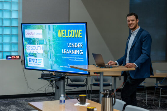 EDC Business Development Officer, Kevin Hatcher, stands at a podium next to a monitor that reads, 'WELCOME LENDER LEARNING' at a lender learning session on August 22nd, 2023 at The HIVE in downtown Grand Forks.
