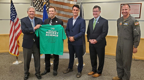 Senator John Hoeven presents a UND t-shirt that reads, "It really is Rocket Science" to Space Development Agency Director Derek Tournear. Standing next to them is Grand Forks Mayor Bochenski, UND President Armacost, and 319th RW Commander Col. Monroe.