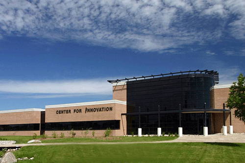 Located in Grand Forks, North Dakota, the side of a building is sitting in front of a blue sky with small clouds. The building sign reads, CENTER FOR INNOVATION.