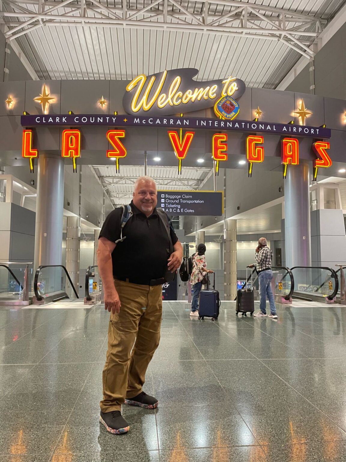 Bill Adams stands in front of a neon sign that reads, Welcome to Las Vegas!