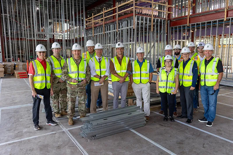 A group of community leaders stand together in construction safety best, hats, and glasses in the new Career Impact Academy building that is under construction.