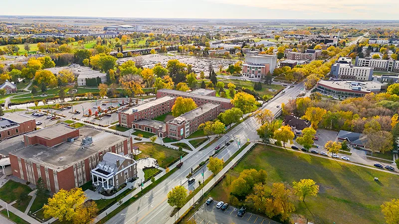 Aerial view of the University of North Dakota campus in autumn, showing tree-lined streets, brick buildings, and parking areas.