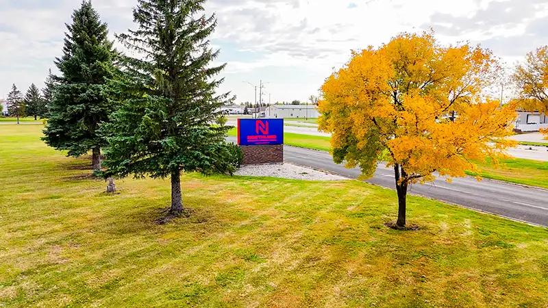 The Northland Community & Technical College sign peaks through between the trees at the front campus entrance in East Grand Forks, Minnesota.