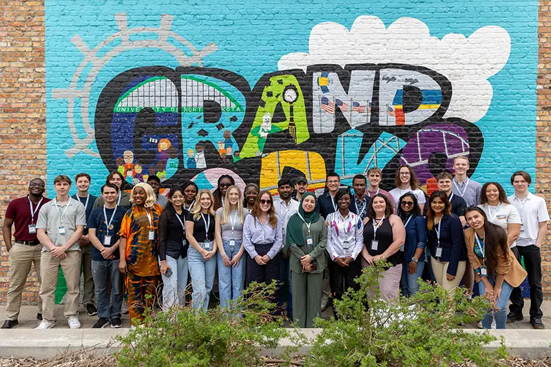 A group of students stand together in front of the Grand Forks mural for the InternGF Summer Cohort Experience.