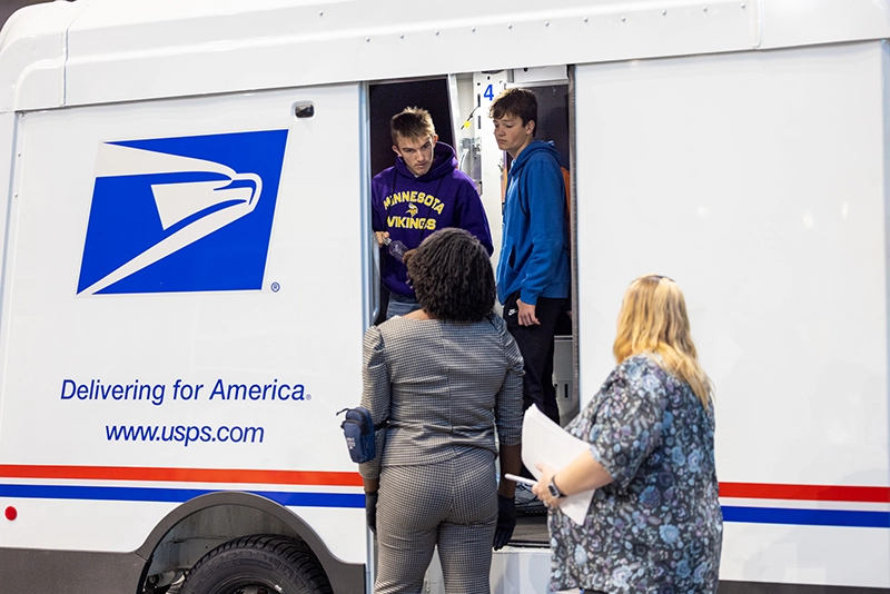 Students and facilitator standing around a United States Postal Service vehicle.