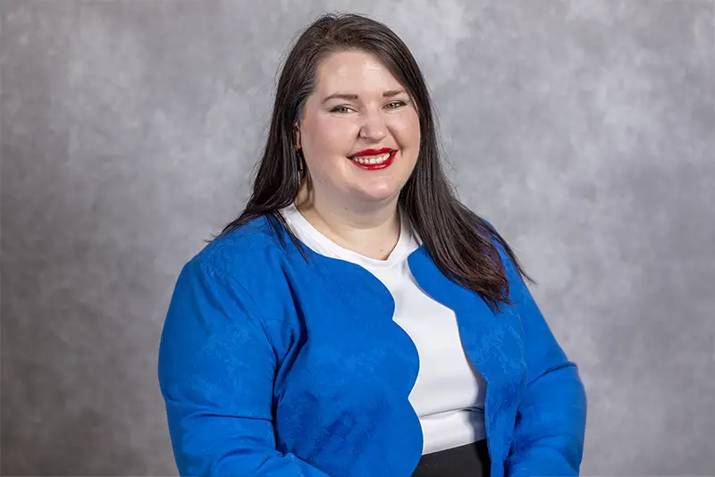 Portrait of Becca Cruger-Schille, EDC Director of Economic Development, smiling in a bright blue jacket against a gray backdrop.