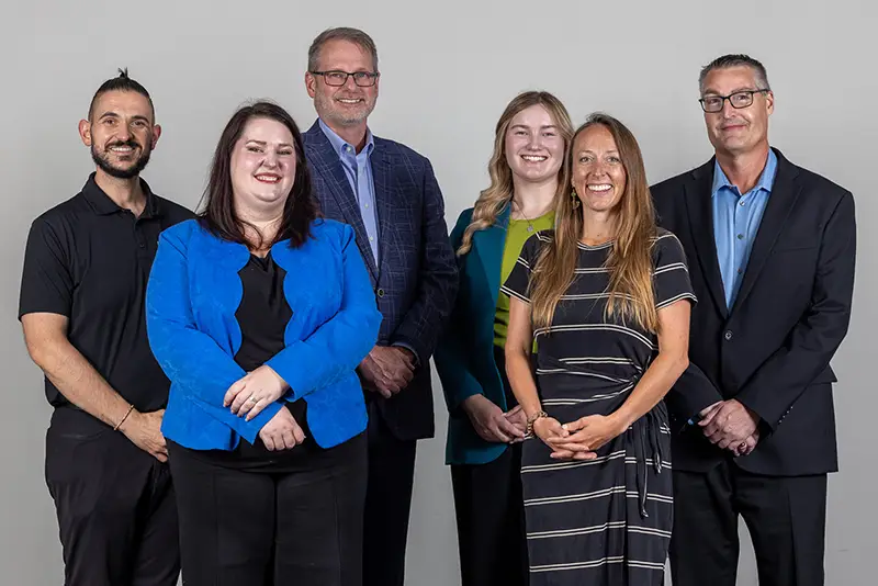 Group portrait of six Grand Forks Region EDC staff members standing together and smiling against a light gray background.
