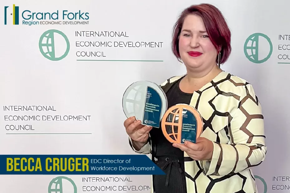 Becca Cruger EDC Director of Workforce Development stands in front of an IEDC step and repeat holding a bronze and silver award.