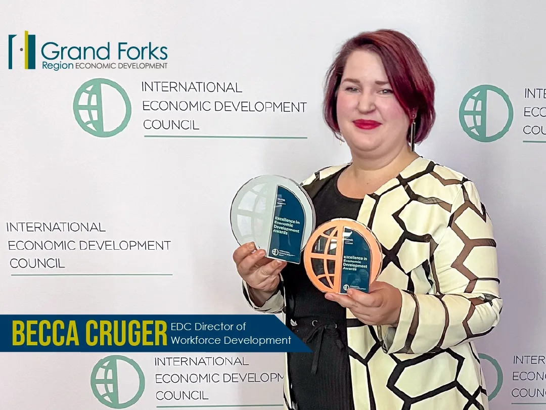 Becca Cruger EDC Director of Workforce Development stands in front of an IEDC step and repeat holding a bronze and silver award.