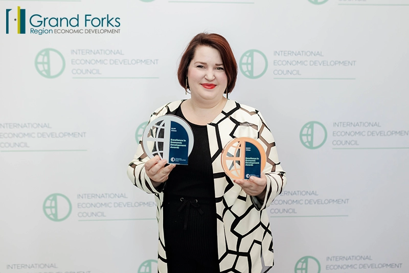 Becca Cruger EDC Director of Workforce Development stands in front of an IEDC step and repeat holding a bronze and silver award.