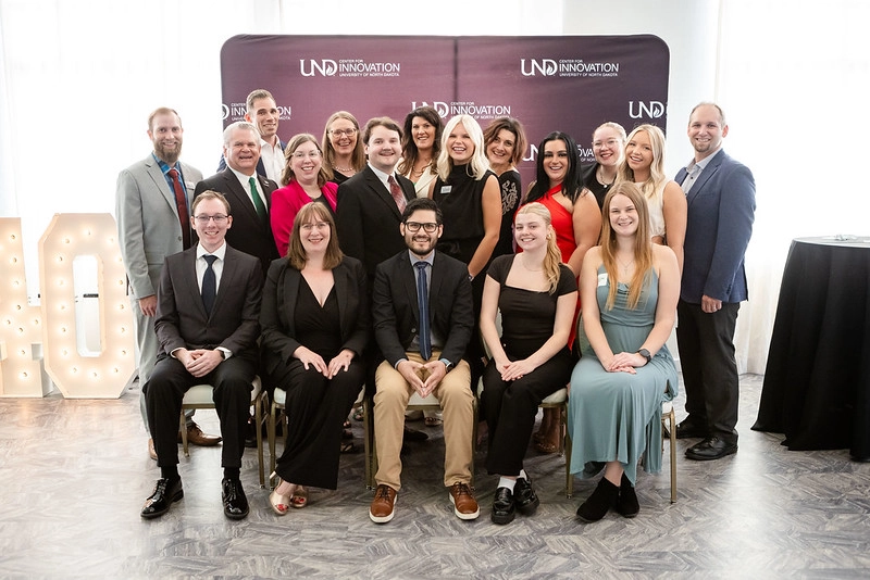 The UND Center For Innovation team pose together in front of the a step and repeat banner of their logo at the 40 year celebration.