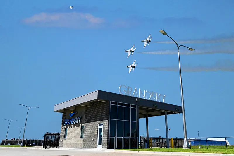 At the entrance to Grand Sky UAS research and development park, three thunderbird airplane fly above.