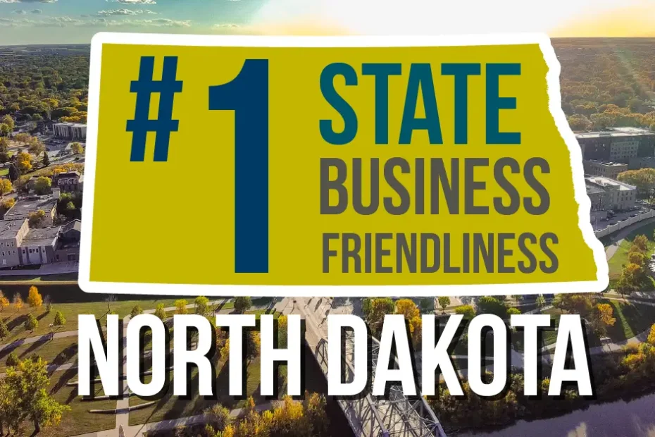 Graphic reading '#1 State Business Friendliness, North Dakota' over an aerial photo of downtown Grand Forks along the Red River in fall, with a pedestrian bridge crossing the water in the foreground.