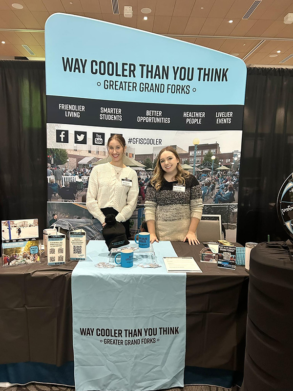 EDC Brenna Mathiason and Meghan Ray stand at the Greater Grand Forks Way Cooler Than You Think! booth at the UND career fair.