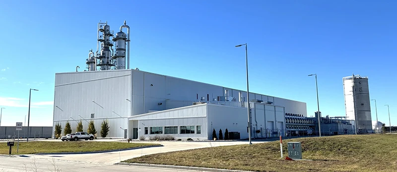 Exterior of the BI Biorefinery, a large light-gray industrial facility with tall distillation columns and a storage tank rising against a clear blue sky.