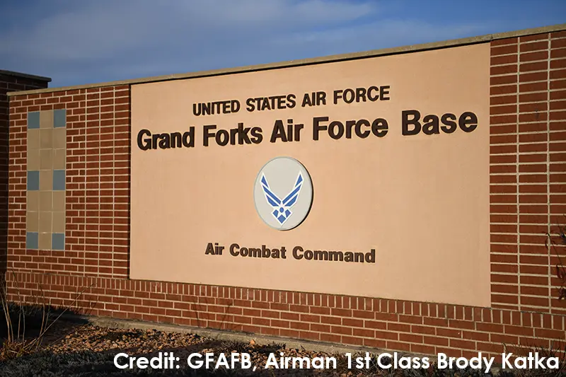 Brick entrance sign for Grand Forks Air Force Base with the U.S. Air Force wings emblem, under a blue sky.